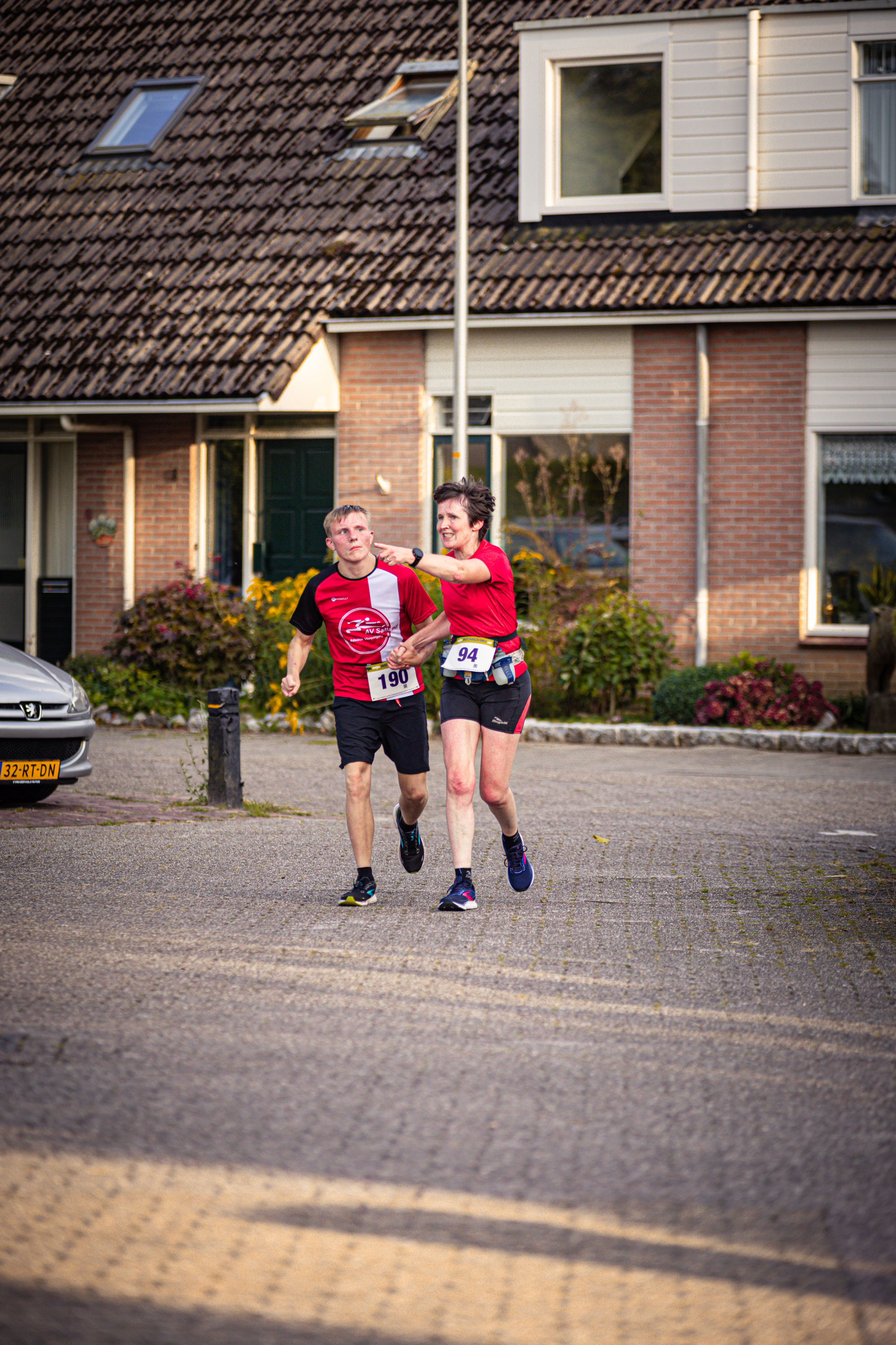 Two runners in red shirts with the word Pomploop on them are running down a street.