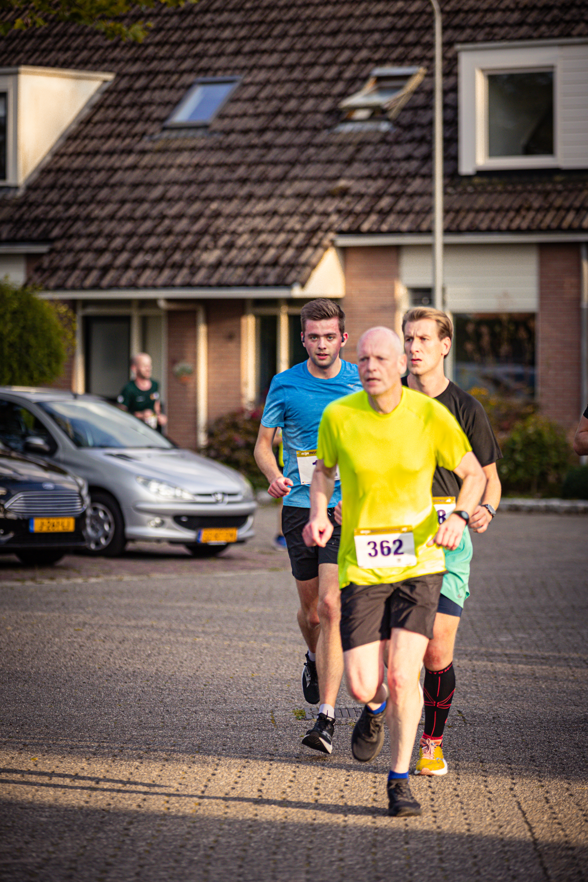 Three men are running in the street, they have numbers on their shirts.