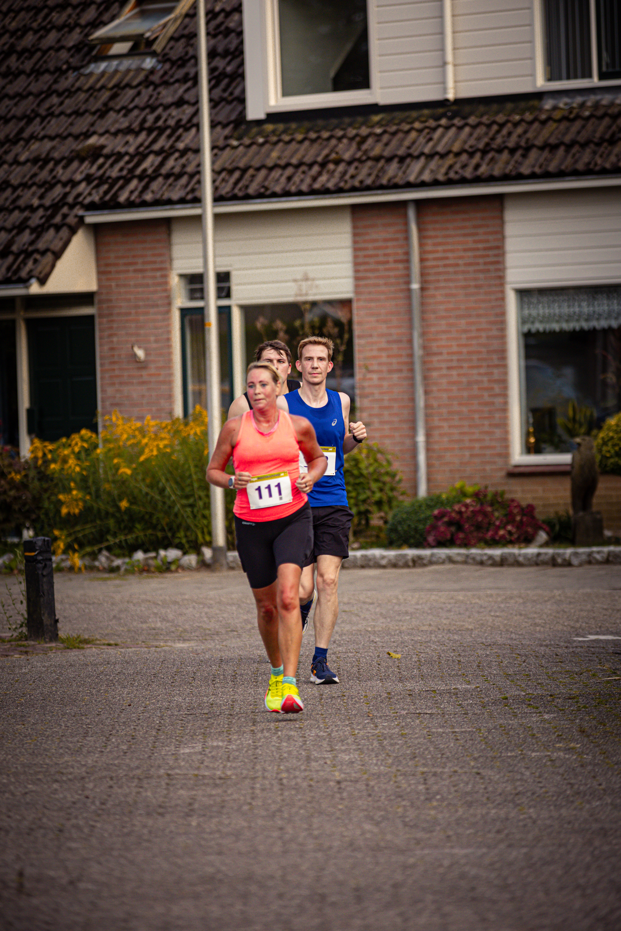 Two people are running on a street, the runner in the front is wearing an orange tank top and has number 11.