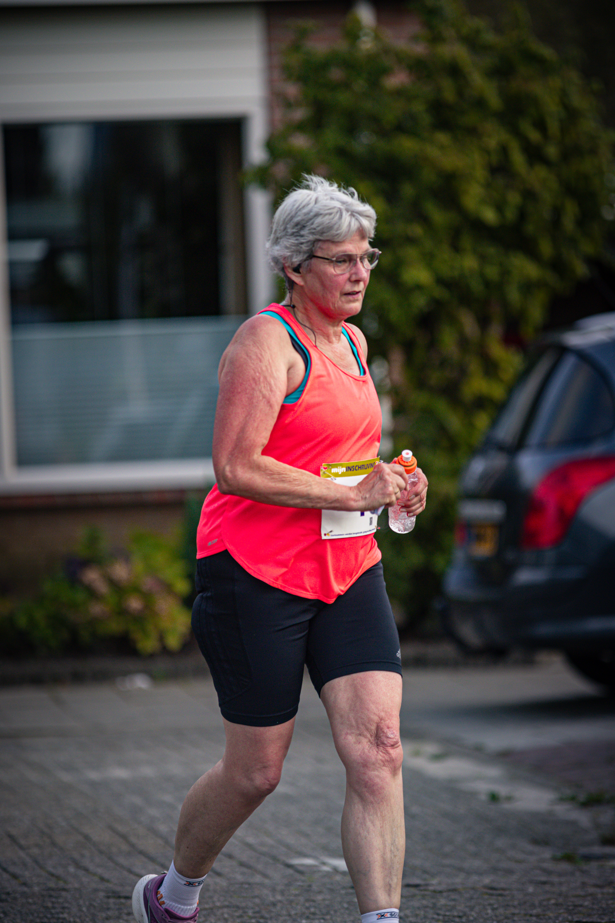 A woman running on a sidewalk while holding a sports bottle in her hand.