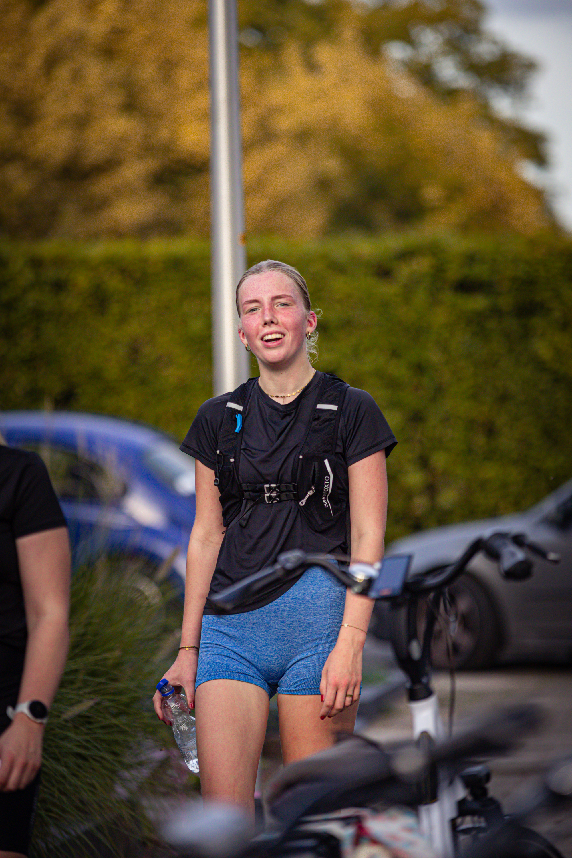 A woman wearing a blue thong is walking her bike next to a car with a blue door handle.