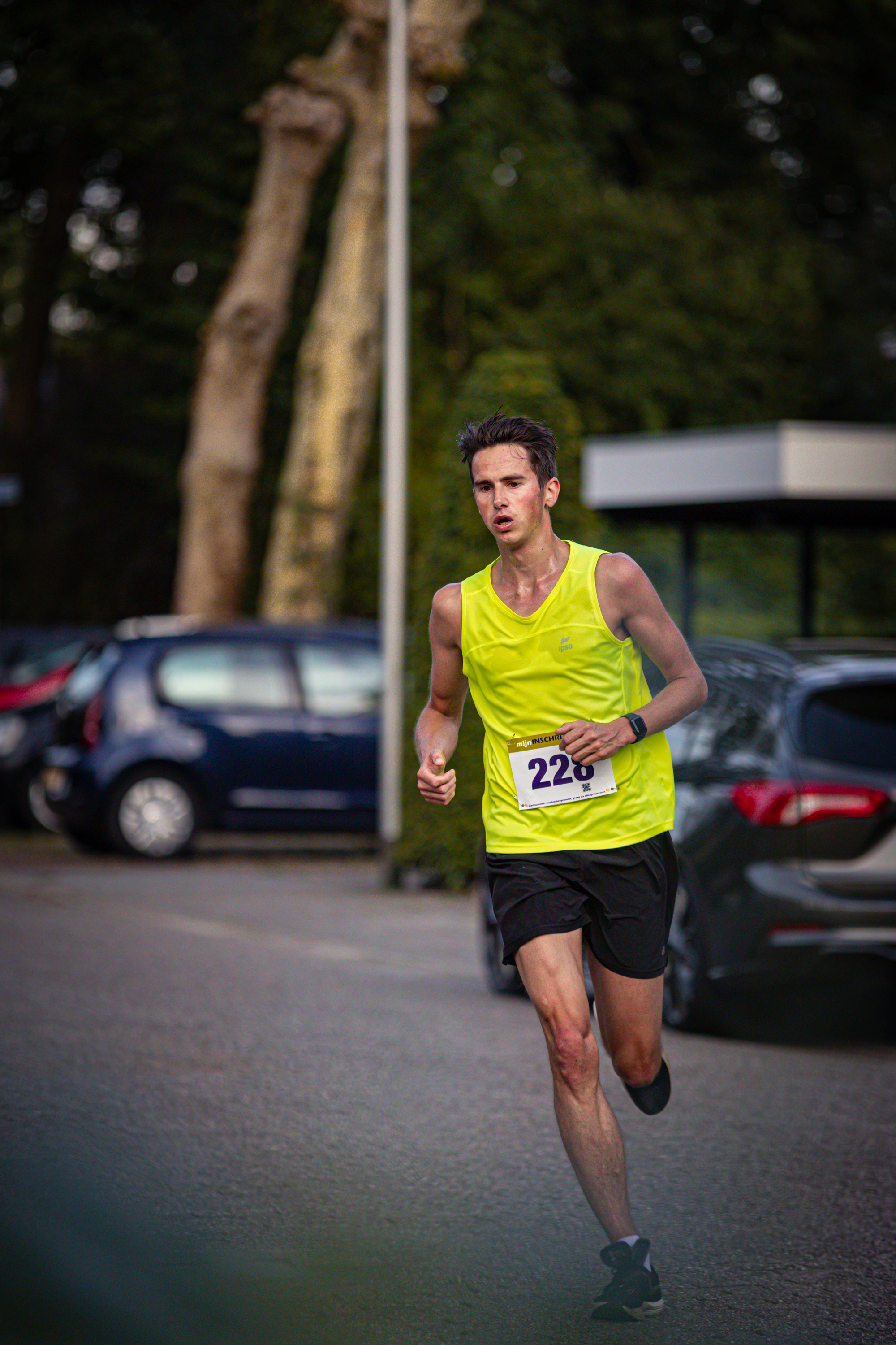 A man is running in the street with a yellow tank top and black shorts.