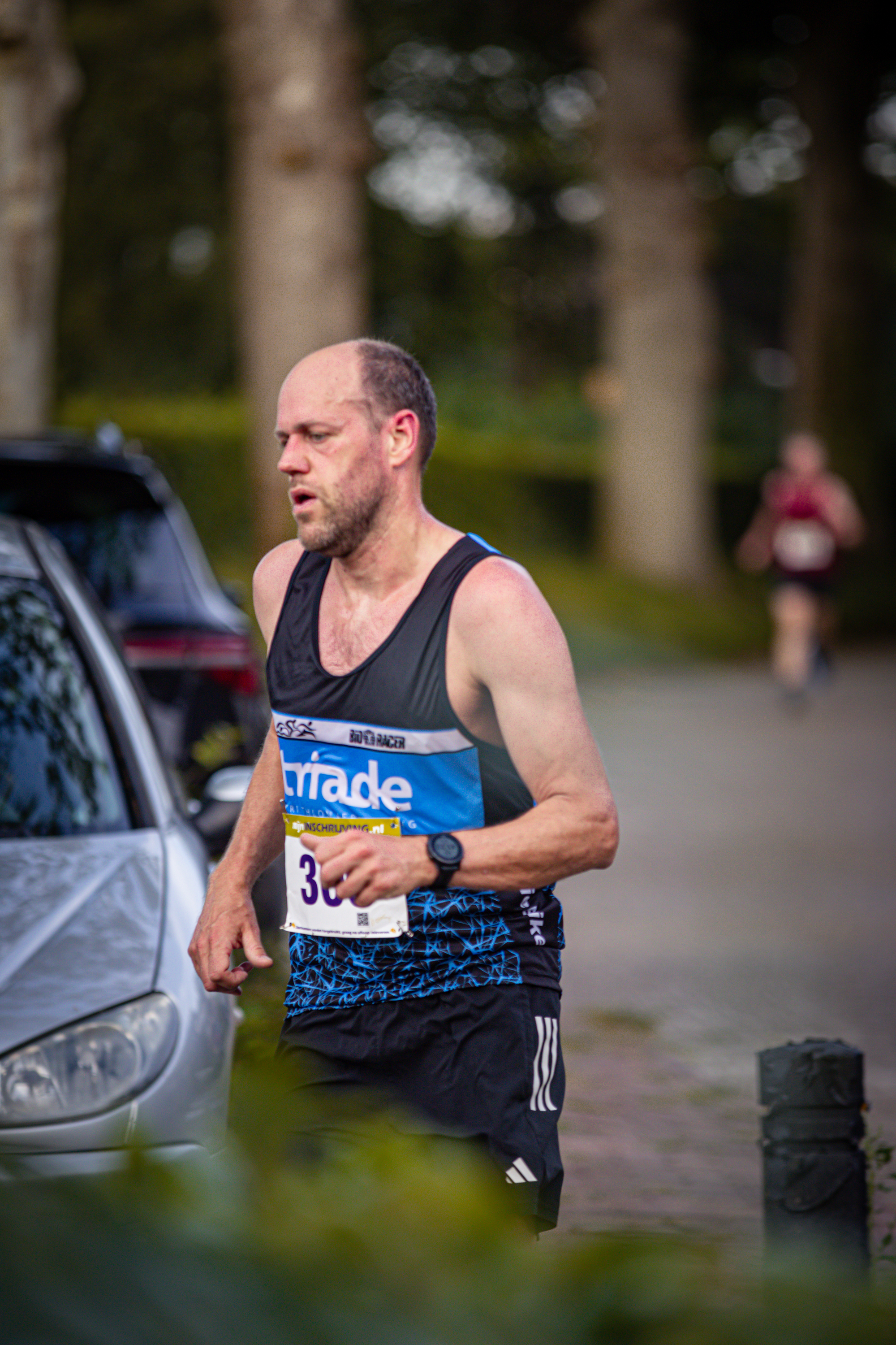 A man in athletic attire runs on a road. He is wearing a bib with the number 3.