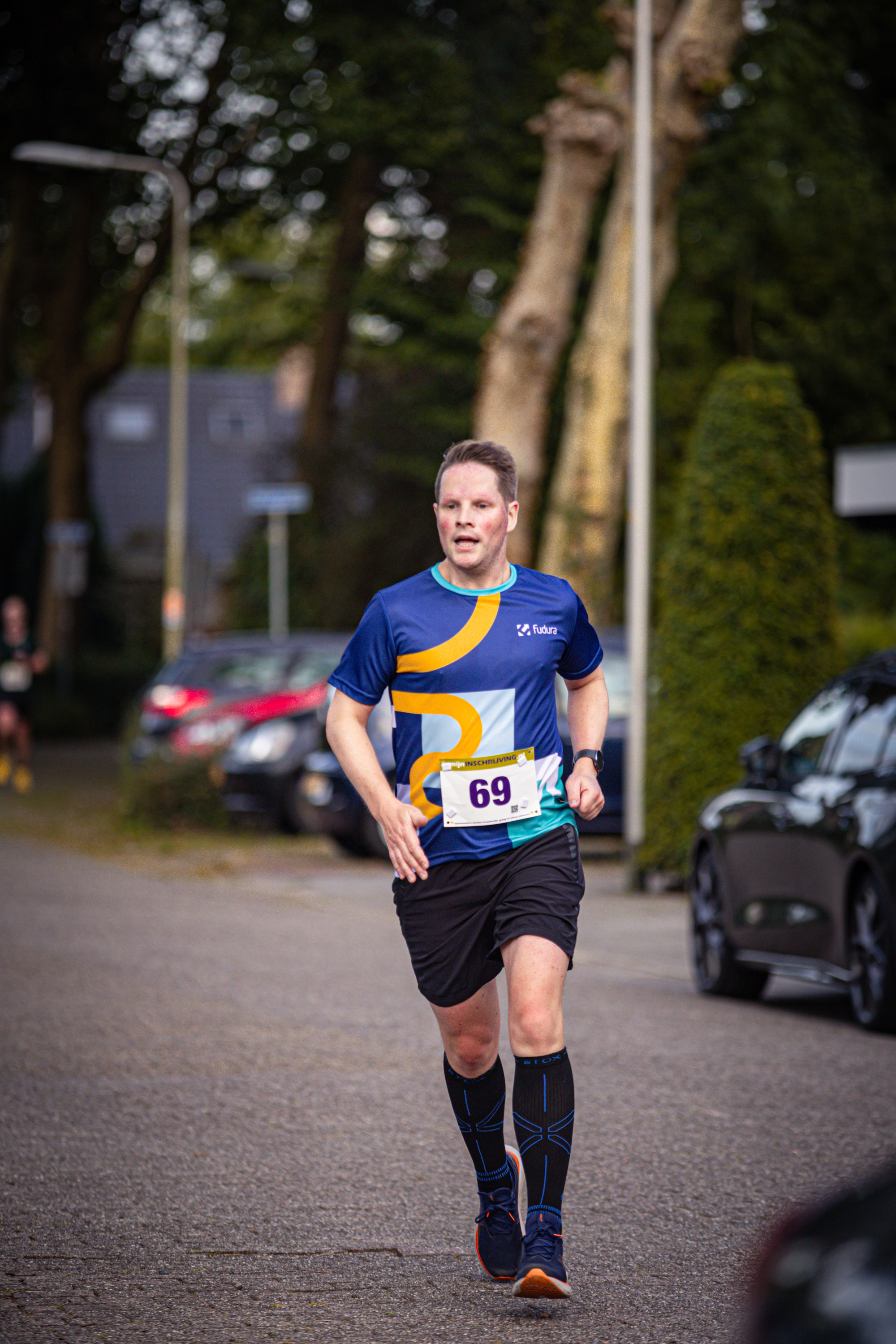 A man running in a blue shirt with yellow numbers on it, and black shorts.