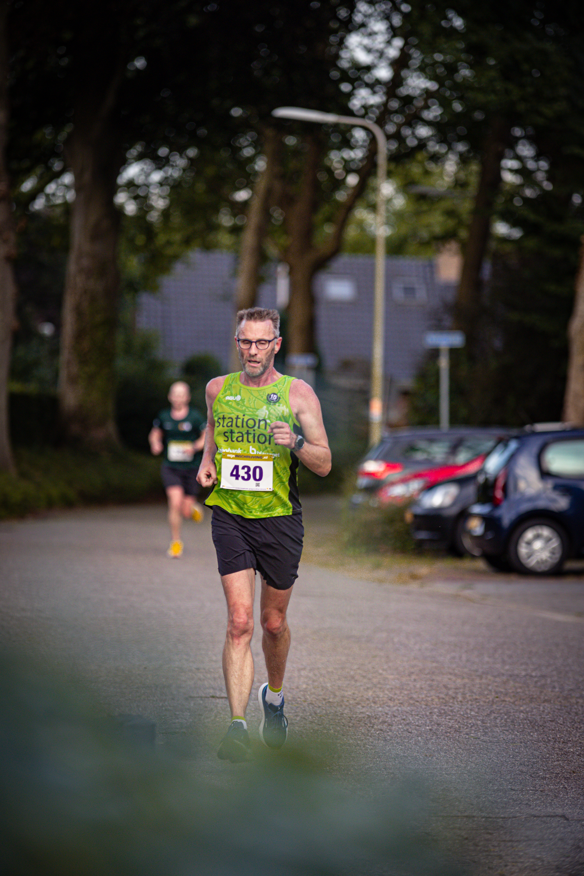 A runner wearing bib number 420 runs down a tree-lined street.