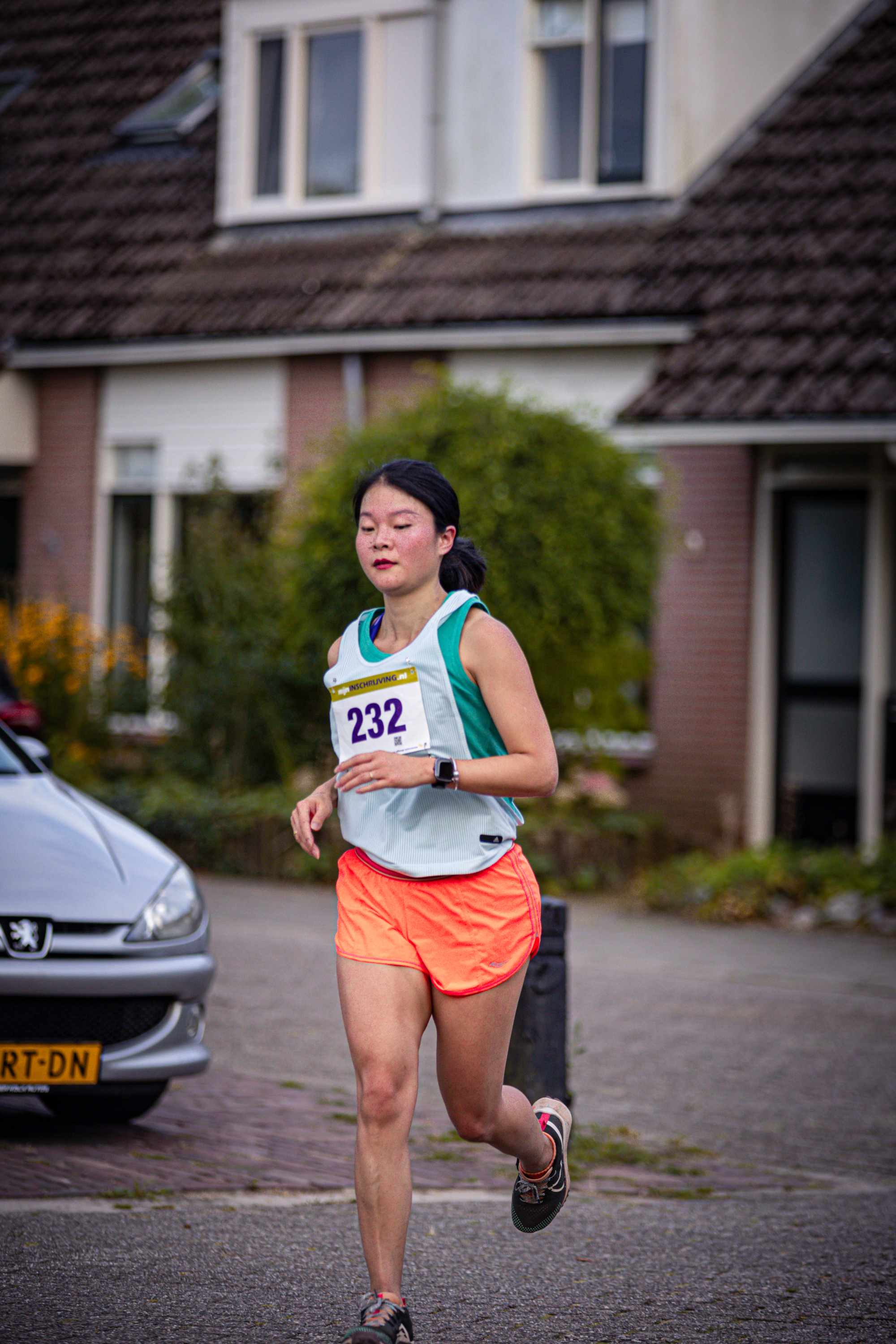 A woman is running down the street with a race bib.