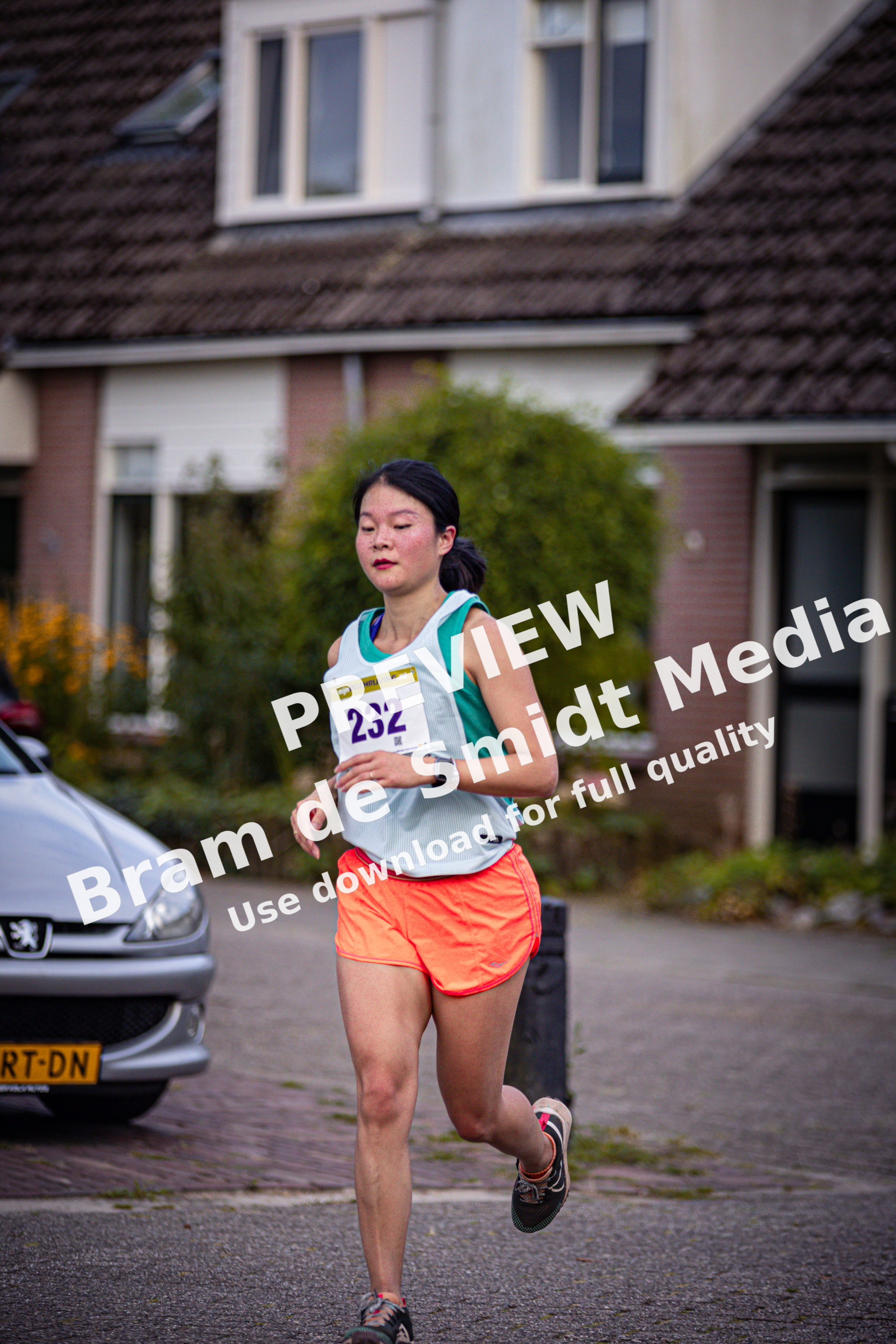 A woman is running down the street with a race bib.