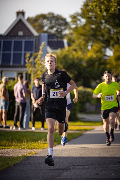 A group of young men are running in a race. The man leading the race is wearing number 21.