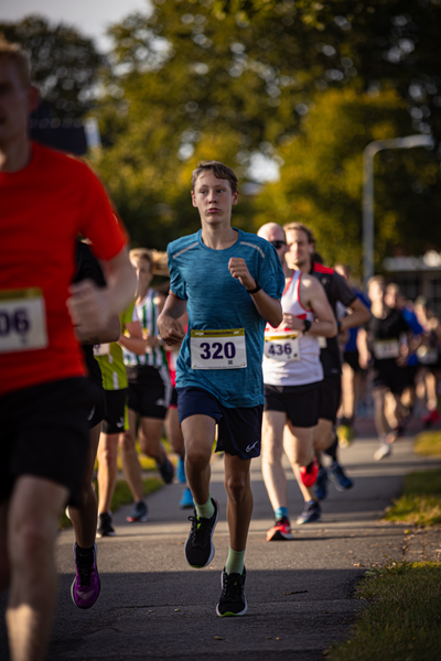 A group of runners are on a path with trees in the background. The runner in the middle wears bib number 320.