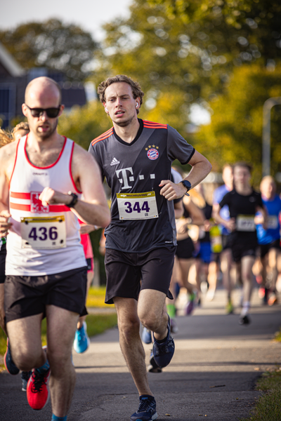 A man wearing a black and red Adidas shirt runs in a race with other runners on the street.