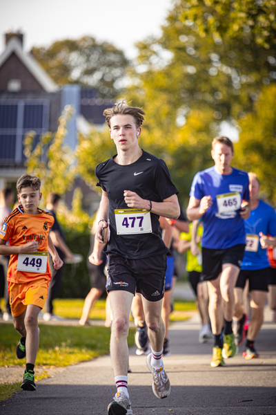 A group of young men running in a marathon on a sunny day. One man wears number 487 and leads the pack.