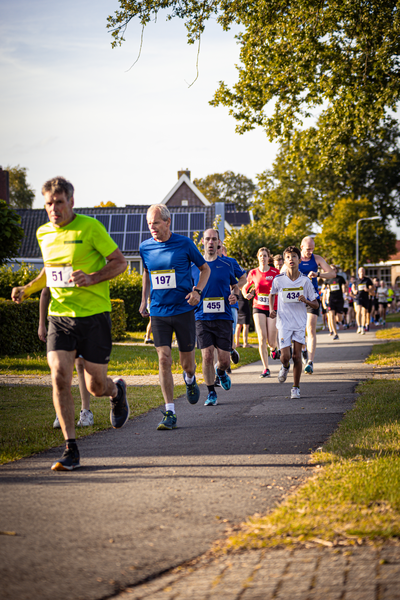 A group of people are running on a paved path, each with numbers pinned to their backs.