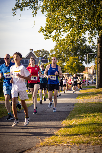 Group of runners with numbered shirts running down a street.