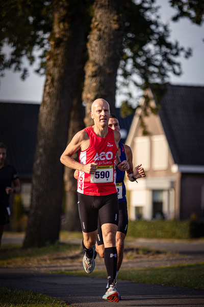 Two runners are wearing numbers 586 and 591 as they run down a street with houses in the background.