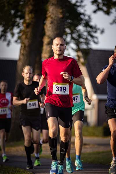 People running on a street with numbers and race bibs on.