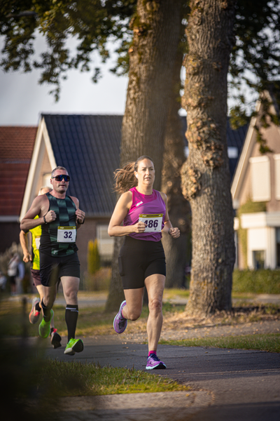 A girl running on a street next to another runner, both wearing bibs with the number 37.