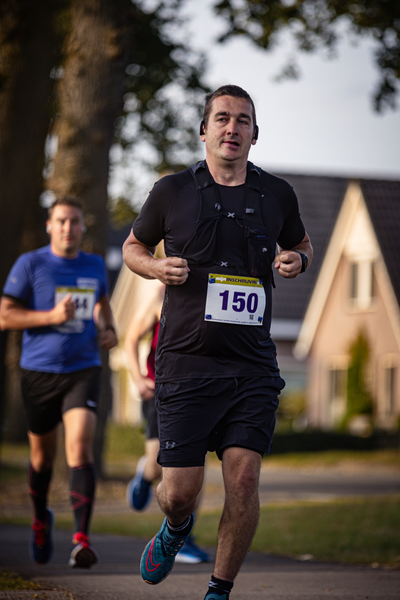 A man running on a street. He is wearing a black shirt and shorts, and has a number 150 on his bib.