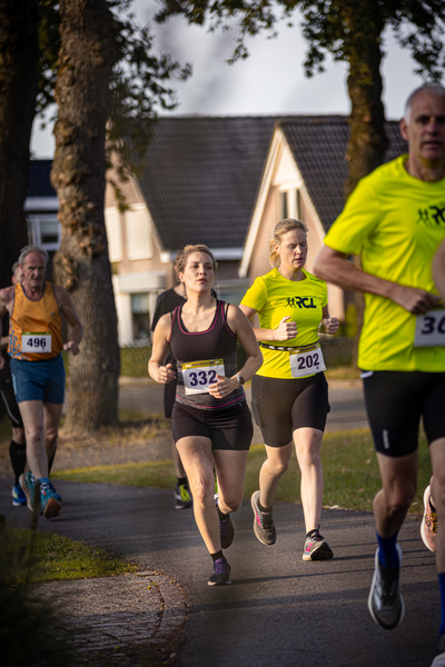 A group of people are running on a sidewalk. The runner in the front is wearing number 32 and has a bib that says "pomp".