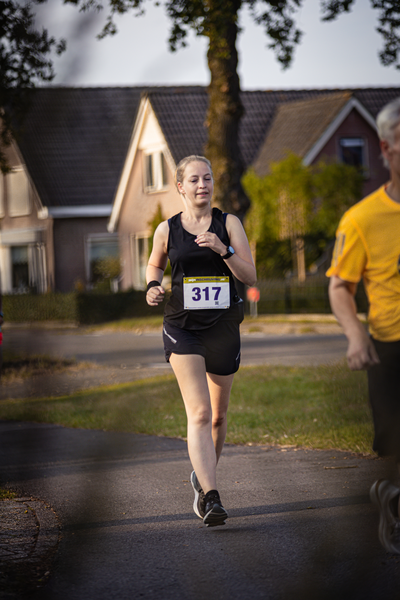 A young woman running in the street wearing black clothing and a 317 tag on her shirt.