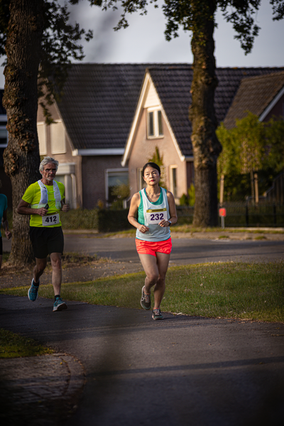 Two runners wearing bibs that say "324" and "4144". They are running on a street with houses in the background.