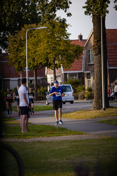 A man is waiting at a crosswalk while running with others. The man has the number 7 on his shirt and a blue hat.