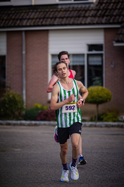 Two people are running down a street. One has 582 on their shirt.