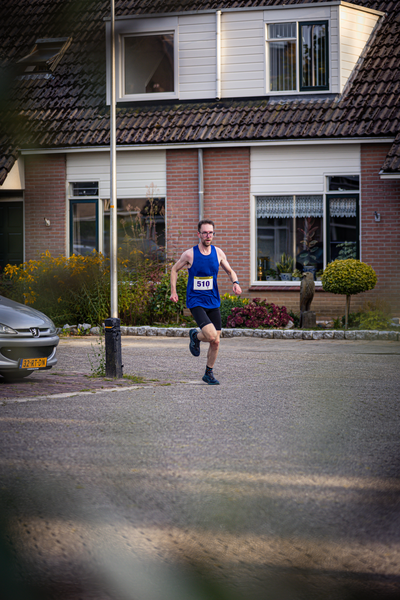 A man running down a street in front of a building and beside a parked car.