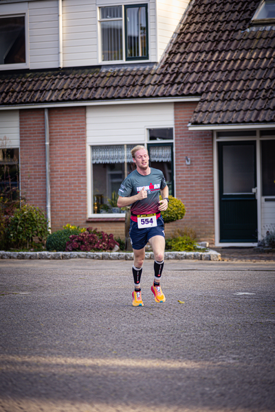 A runner in a black shirt, shorts and red sneakers carrying a water bottle and wearing the number 939.