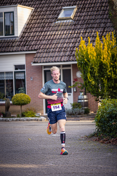 A man runs across a street, wearing a Pomploop shirt.