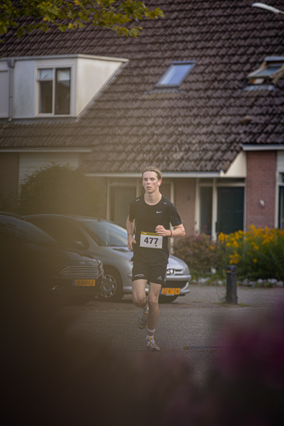 A man running with a number 327 on his shirt. He's wearing black shorts and is looking towards the right side of the image.