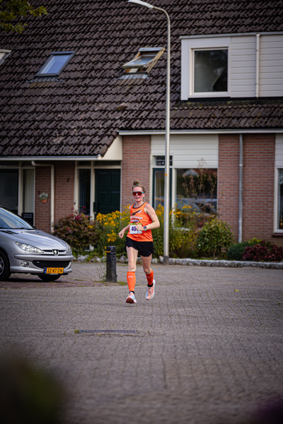 A woman running on the street wearing an orange top and black shorts.