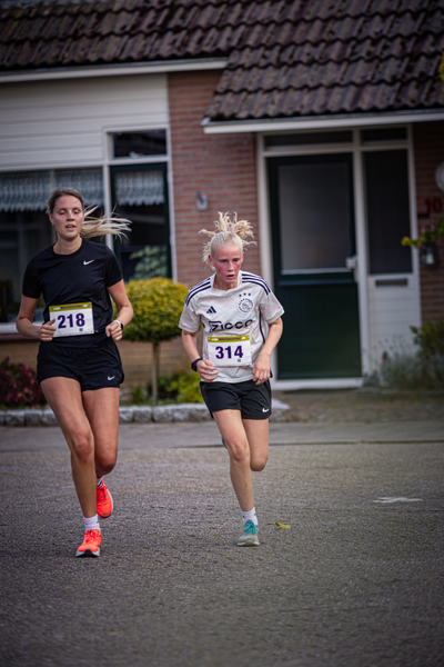 Two women are running in front of a brick building.