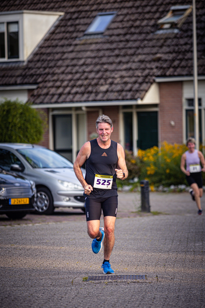 A man wearing a black tank top and blue shorts running down the street.