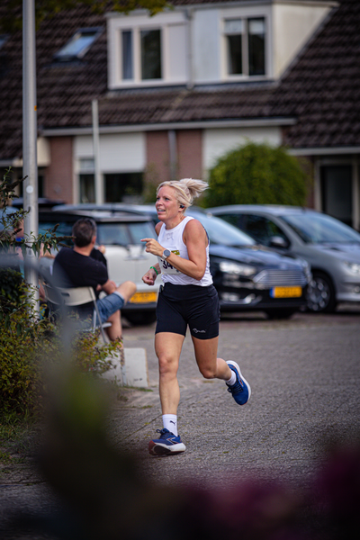 A woman running in the street wearing a white tank top and black shorts.