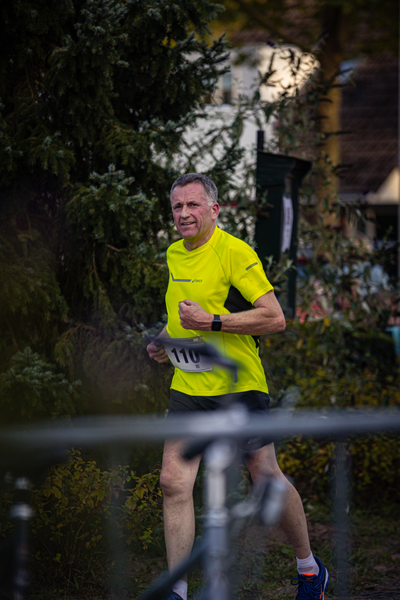 A man wearing a yellow Pomplosh shirt is running with his arms and legs spread out.