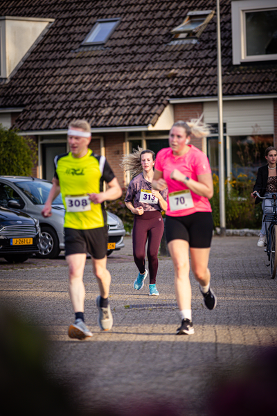 A woman runs in a race, wearing a pink tank top. She is passing another runner who is running in the opposite direction.