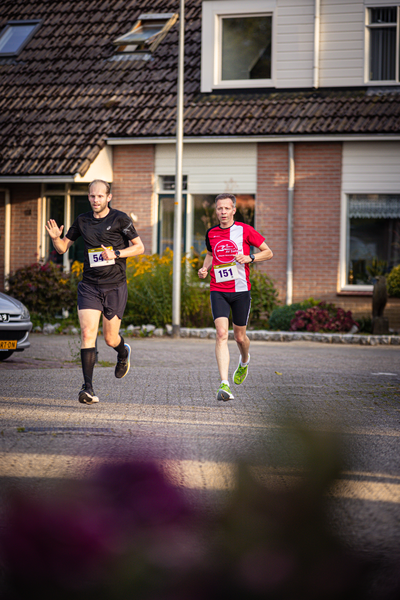 Two people running in a street with one wearing a shirt that says "Pomploop".