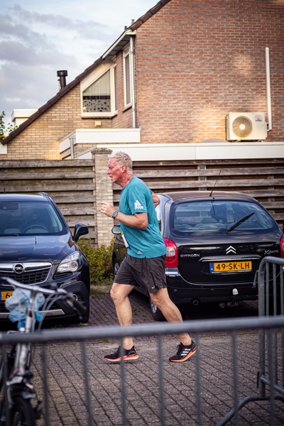 A man wearing a green shirt and blue shorts is running with a black sports bag on his shoulder.