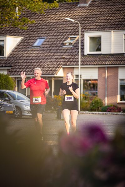 A man is running down a street in front of a house with his wife.