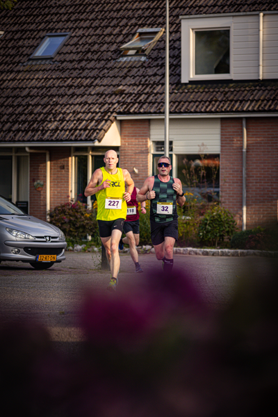 A man running in a race on a street in front of a car and a building.