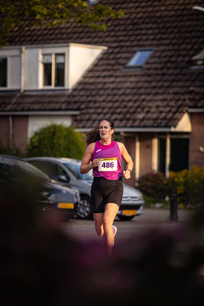 A woman is running in a park with 486 written on her shirt.