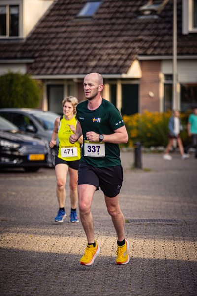 A man and a woman are running in a parking lot. The man is wearing the number 437 on his shirt.