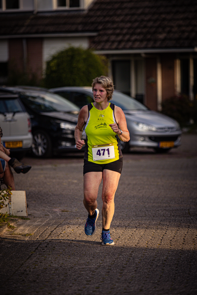 A woman running with a yellow shirt and blue shorts in front of cars.