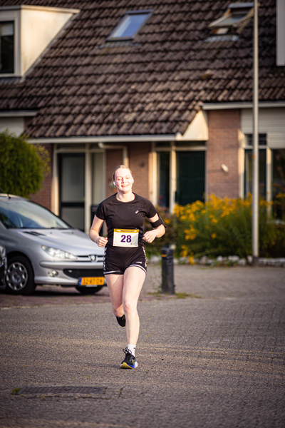 A woman running in the street with the number 28 on her shirt. She is wearing shorts and a black top.