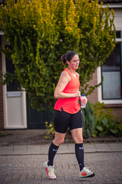 A woman in an orange shirt and black leggings is jogging outside.