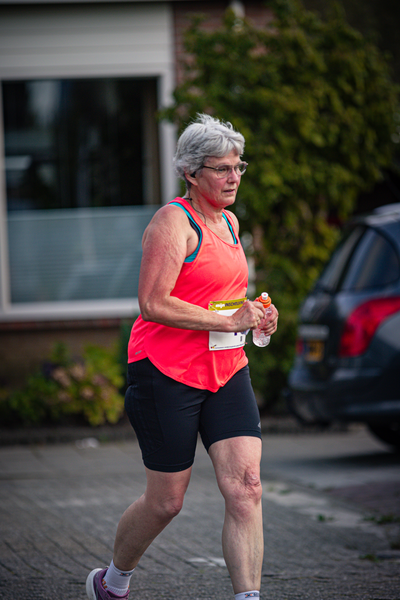 A woman running on a sidewalk while holding a sports bottle in her hand.