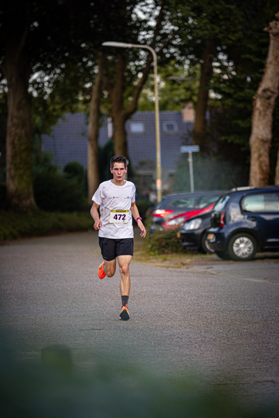 A man is running on a street. He has the number 487 on his shirt and an orange band on his wrist.