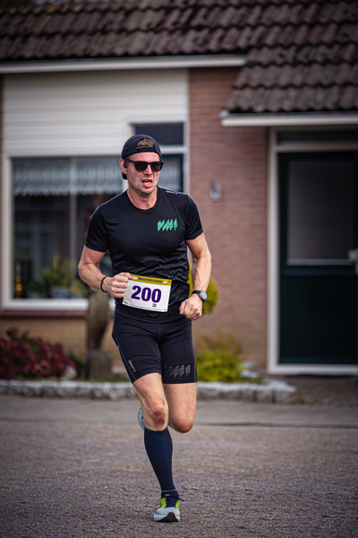 A man wearing a black shirt and shorts with the number 200 on his right arm, and running.