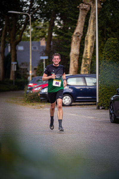 A man wearing a green tank top with the number 8 on it runs down the street.