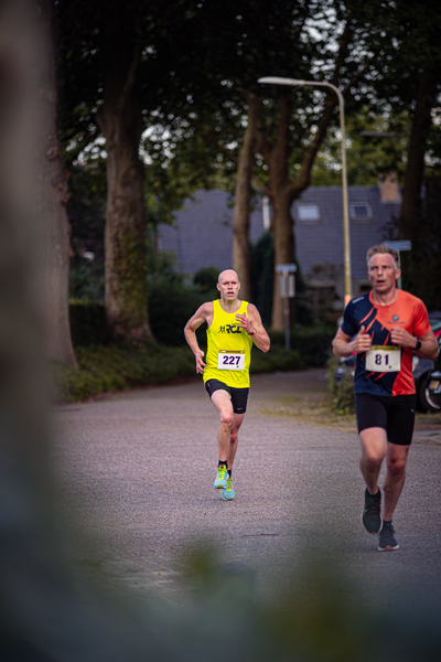 Two runners wearing numbered bibs on a city street at dusk. One of them has the number 32.